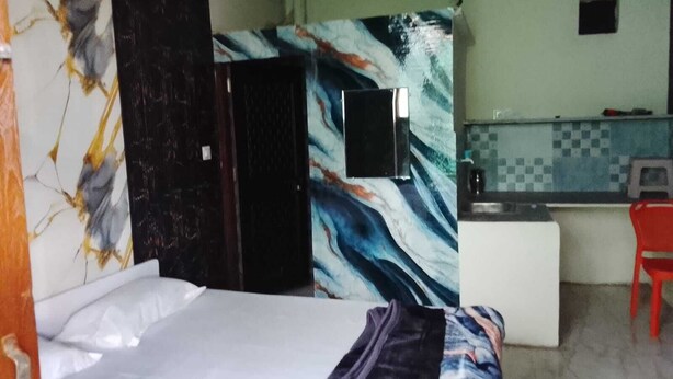 Una habitación con cama, televisión en la pared, una pequeña kitchenette y una silla roja.