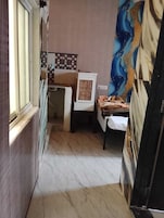 A narrow corridor leading to a room with a bed, a chair, and a small table.