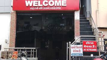 A hotel entrance with a red sign reading 'HOTEL WELCOME' and a signboard with contact information.