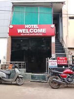 Entrada de un hotel con un letrero rojo que dice 'HOTEL WELCOME' y una placa con información de contacto.