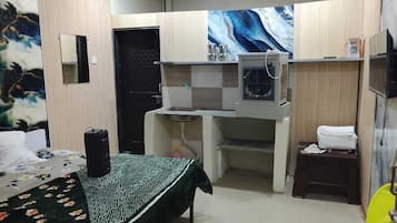 A compact room with a bed, a small kitchenette, a bathroom, and a shower area.