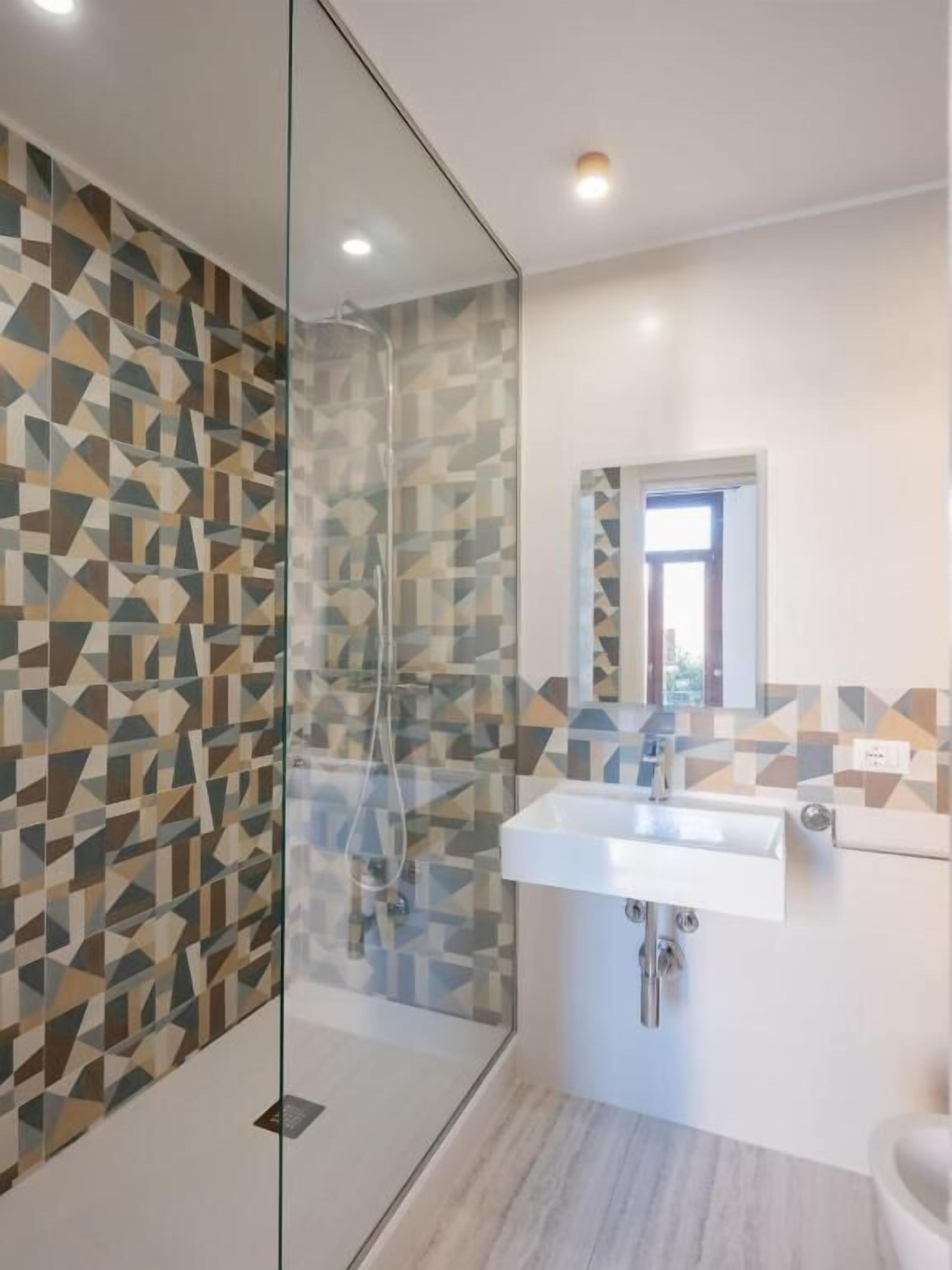 A modern bathroom with a glass shower enclosure, a white sink, and a geometric patterned wall.