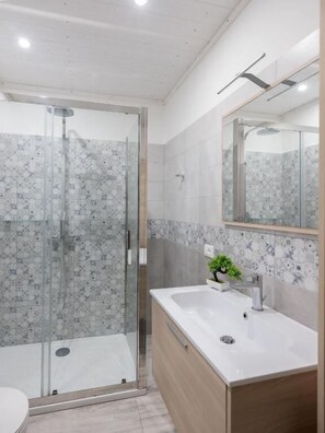 Un baño moderno con ducha envuelta en vidrio, un lavabo blanco y un mueble de tocador de madera.