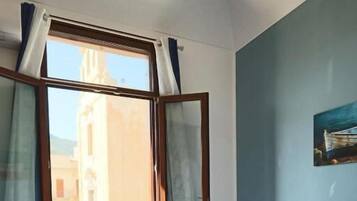 Una camera da letto con un letto, due cuscini, una finestra con tende e vista sugli edifici.