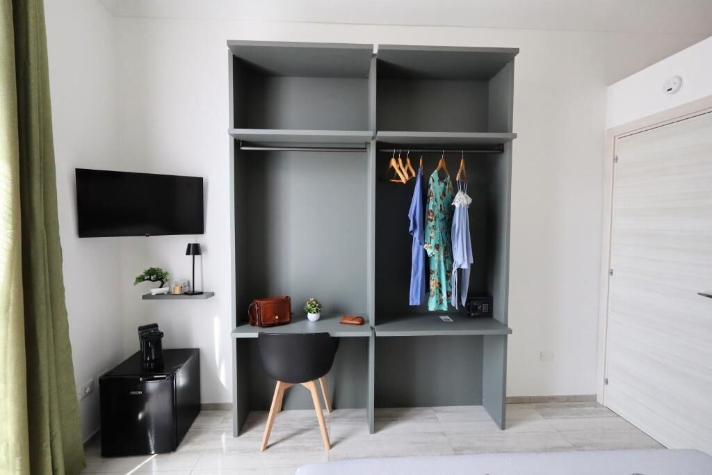 A modern room with a grey wardrobe, a desk, a black chair, a television, and a white door.