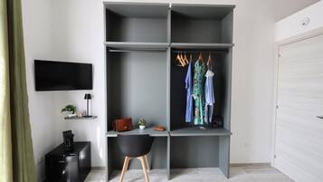 A modern room with a grey wardrobe, a desk, a black chair, a television, and a white door.