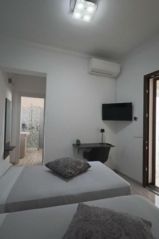 A bedroom with two beds, a mounted TV, a bedside table, and an air conditioning unit.