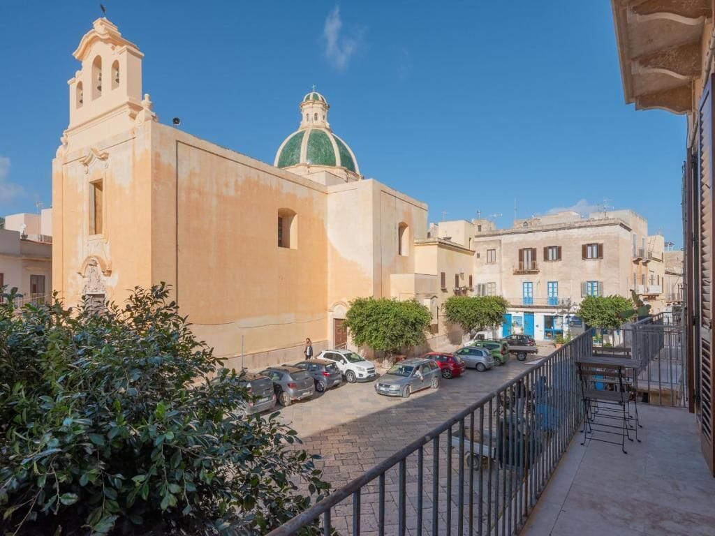 Una vista di strada con una chiesa caratterizzata da una cupola verde e un campanile, auto parcheggiate e un percorso pedonale.