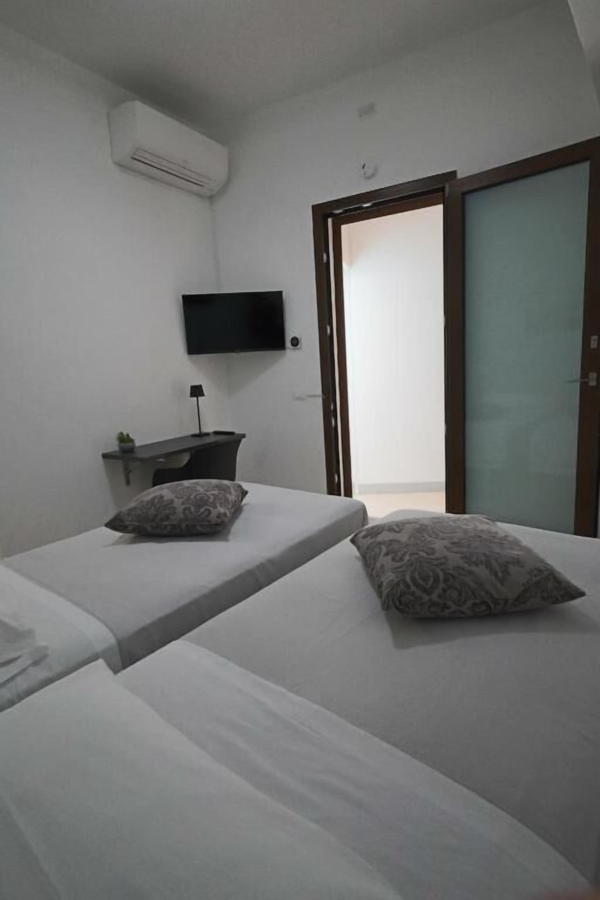 Een hotelkamer met twee bedden, een flatscreen televisie aan de muur, een klein tafeltje met een lamp en een schuifdeur naar een balkon.