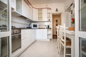 A kitchen with white cabinets, a microwave, a stove, and a dining area with a white chair and table. - la casetta di ili e giuly (Fiumicino)