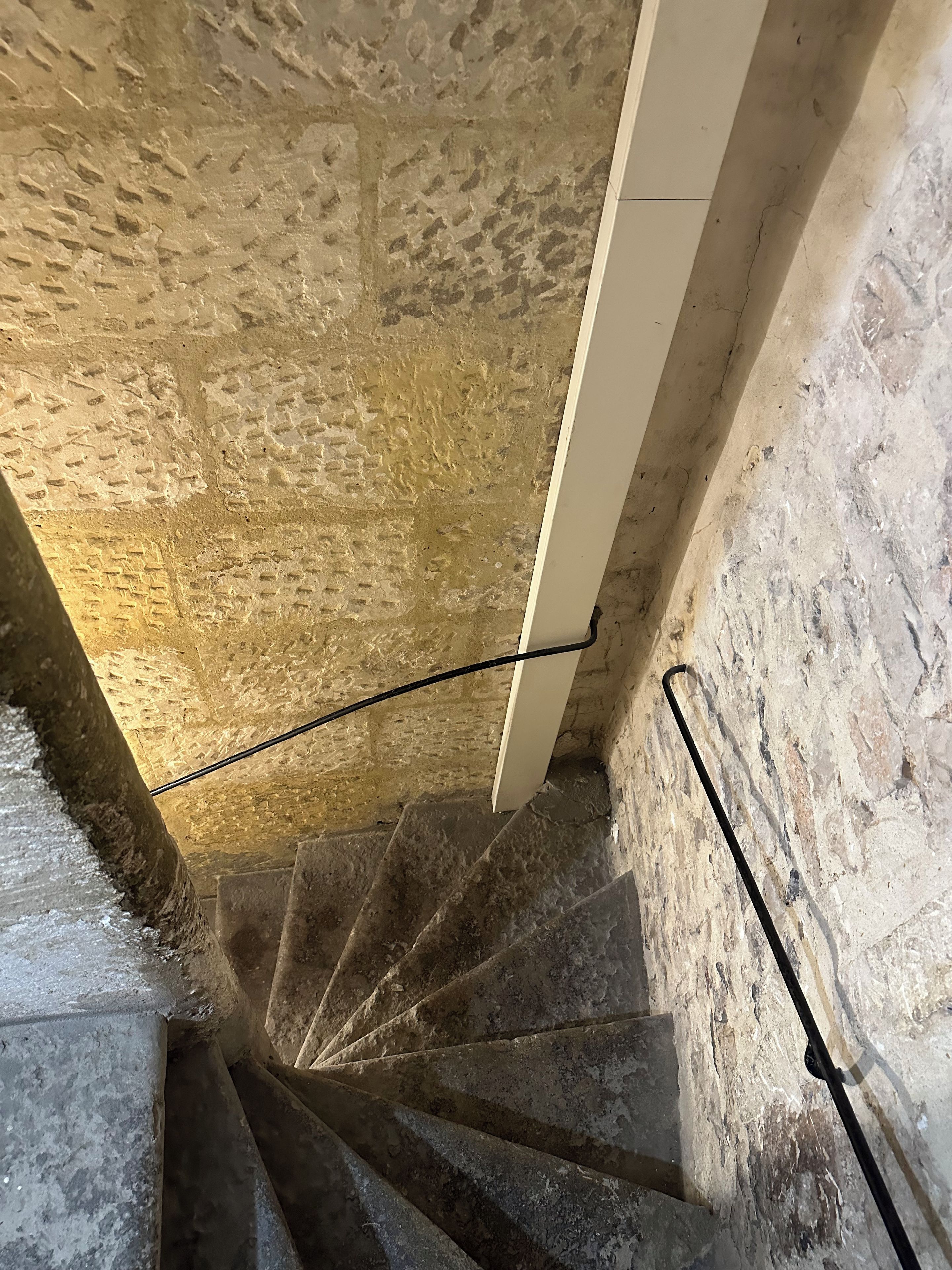 A spiral staircase with stone walls and a metal handrail.