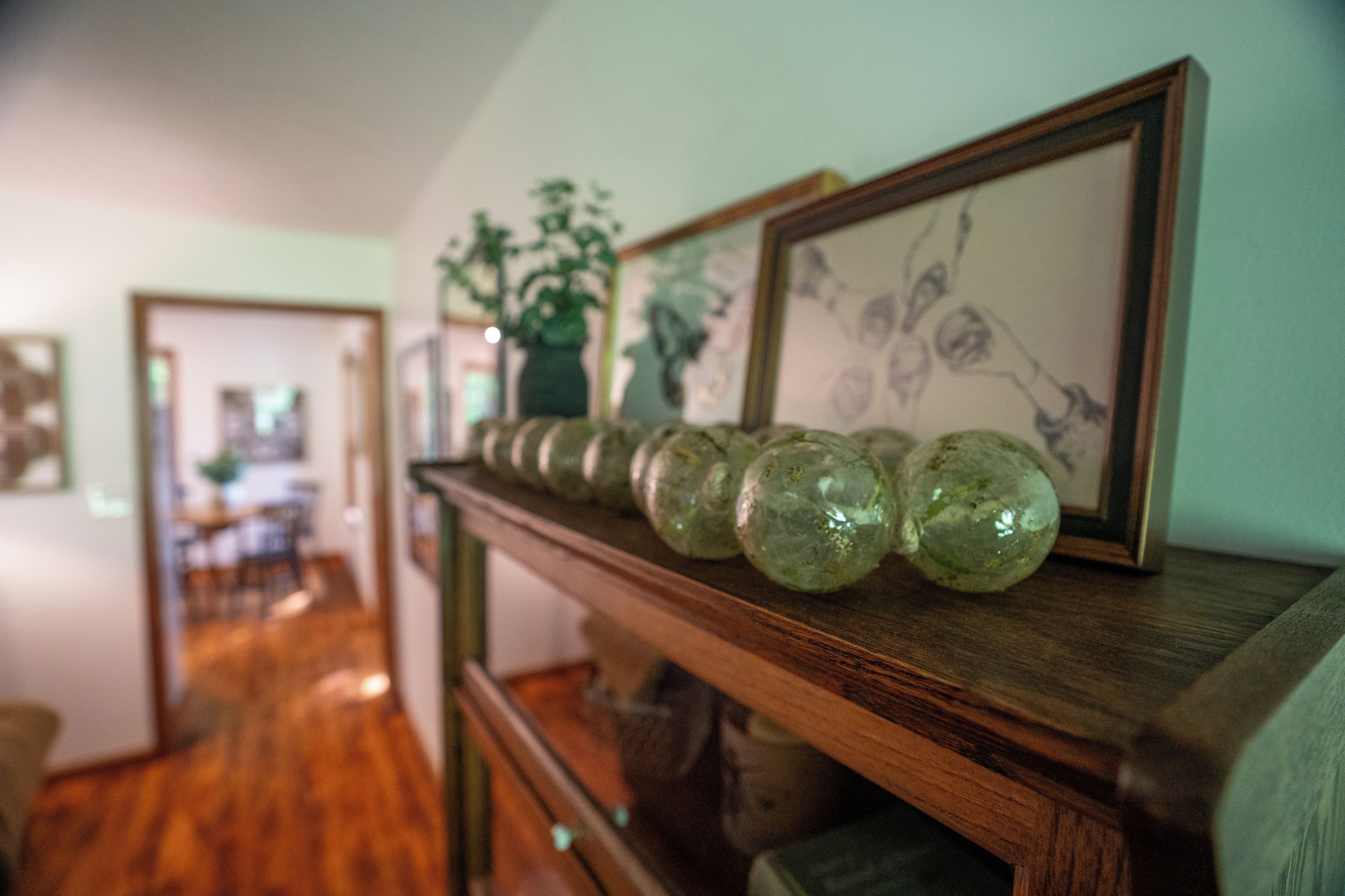 Un pasillo con un banco de madera que exhibe objetos de vidrio verde y obras de arte enmarcadas.