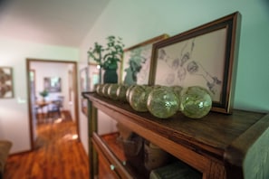 A hallway with a wooden bench displaying green glass objects and framed artwork.