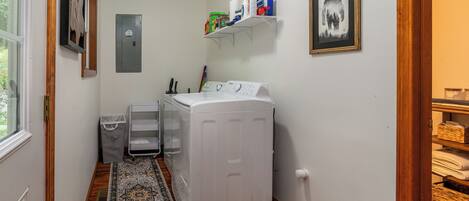 A laundry room with a washing machine, a drying rack, and shelves with cleaning supplies.