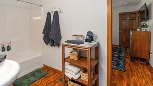 Ein Badezimmer mit einer Badewanne, einer Toilette, einem Waschbecken und einem Waschtisch mit Spiegel. Handtücher und eine kleine Ablagefläche mit Pflegeprodukten sind vorhanden.