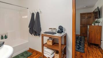 A bathroom with a bathtub, a toilet, a sink, and a vanity with a mirror. There are towels and a small shelf with toiletries.