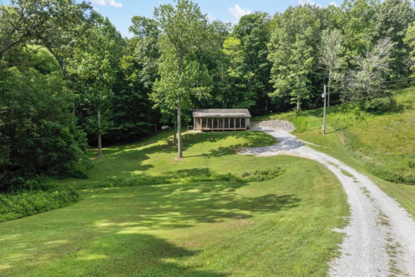 A building with a simple, rectangular structure, surrounded by a natural landscape with trees and a gravel path leading to it.