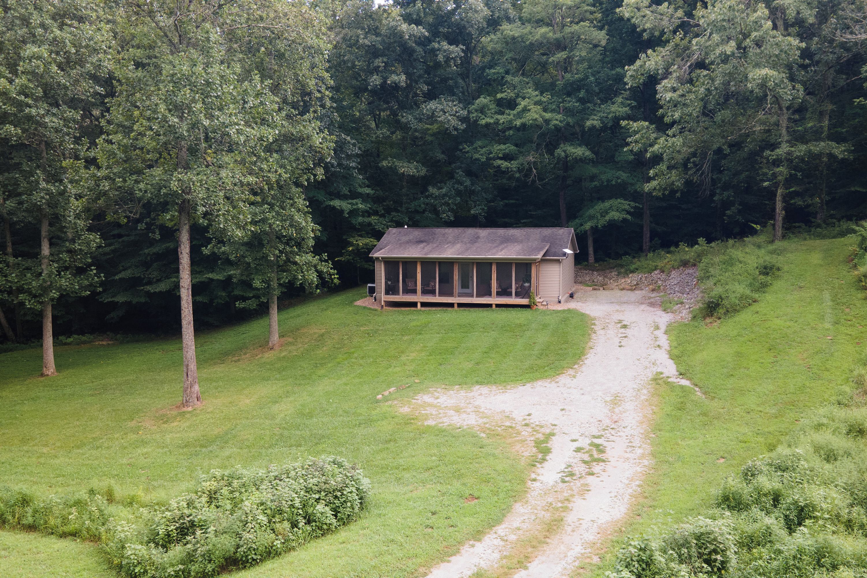 A secluded cabin surrounded by dense forest, accessible by a narrow dirt path.