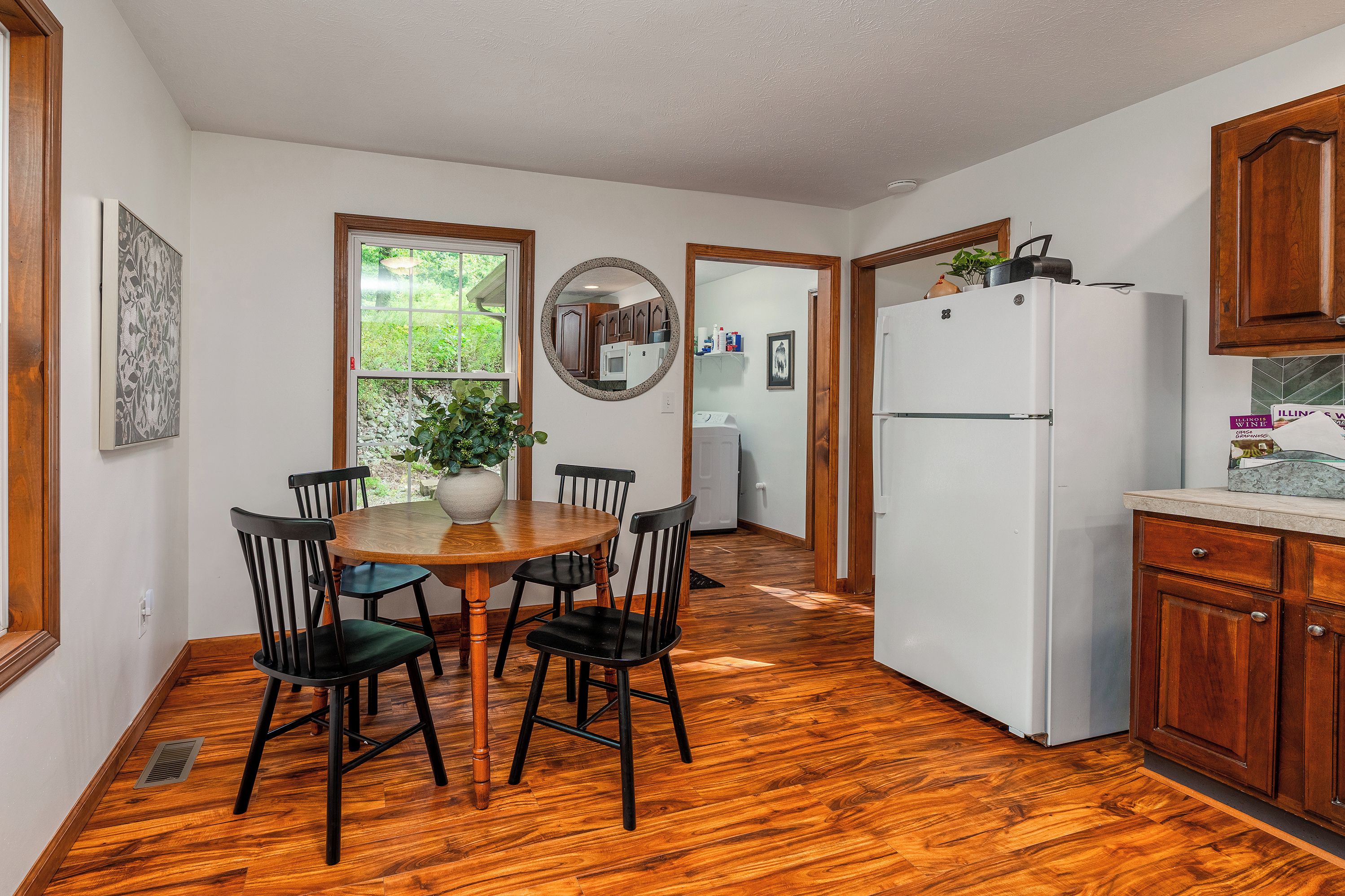 A kitchen with a dining table, chairs, a refrigerator, and wooden cabinets.