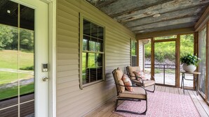A covered porch with a wooden floor, a cushioned chair, and a potted plant.