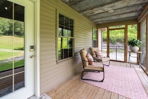 A covered porch with a wooden floor, a cushioned chair, and a potted plant.
