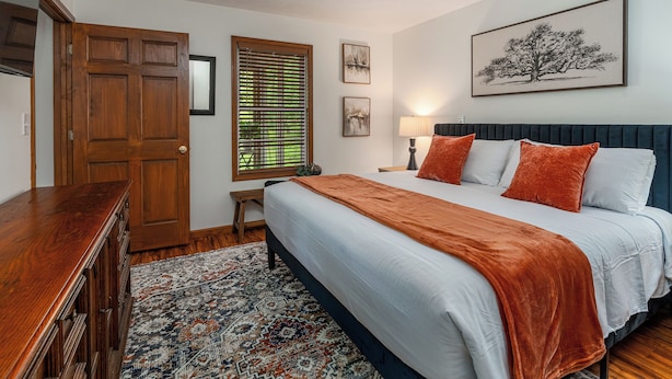 A bedroom with a bed, a nightstand, a lamp, a window with blinds, a door, and a rug.