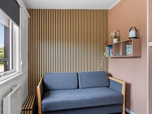 Ein Zimmer mit einer grauen Couch, einer Wand aus Holzlatten, einem Heizkörper und einem Regal mit Büchern und einer Pflanze.