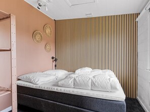 Une chambre à coucher de taille réduite, comprenant un lit, une étagère fixée au mur et un mur décoré de lambris.