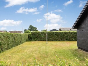 A grassy backyard with a tall metal pole, a hedge, and a building with a dark exterior. - "Solvey" - 700m from the sea by Interhome (Hejls)