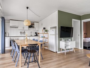 A modern kitchen with white cabinets, a dining table with chairs, and a TV in the living area. - "Solvey" - 700m from the sea by Interhome (Hejls)