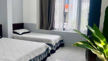 A hotel room with two beds, a window with curtains, a plant on a table, and a vase.