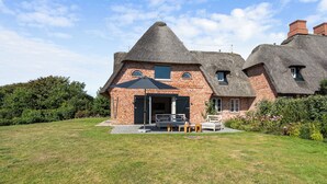Une maison avec un toit de chaume, des murs en briques et un petit jardin agrémenté de mobilier d’extérieur.