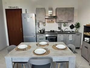 A modern kitchen with grey cabinets, a stainless steel refrigerator, and a dining area set with four plates and cutlery. - La Pigna delle Aci Apartment (Acireale)