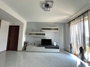 A modern living room with a flat-screen TV, built-in shelves, and a decorative light fixture. - La Pigna delle Aci Apartment (Acireale)