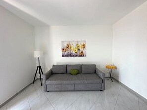Uma sala de estar moderna com um sofá cinzento, um abajur e uma obra de arte na parede.