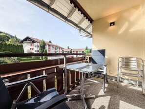 Ein Balkon mit Metalltisch und -stühlen, Blick auf Häuser und einem klaren Himmel.