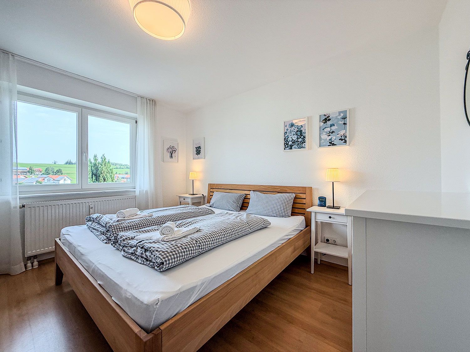 Un dormitorio con una cama grande, dos mesitas de noche, una mesita auxiliar, una ventana con vistas y decoración en la pared.
