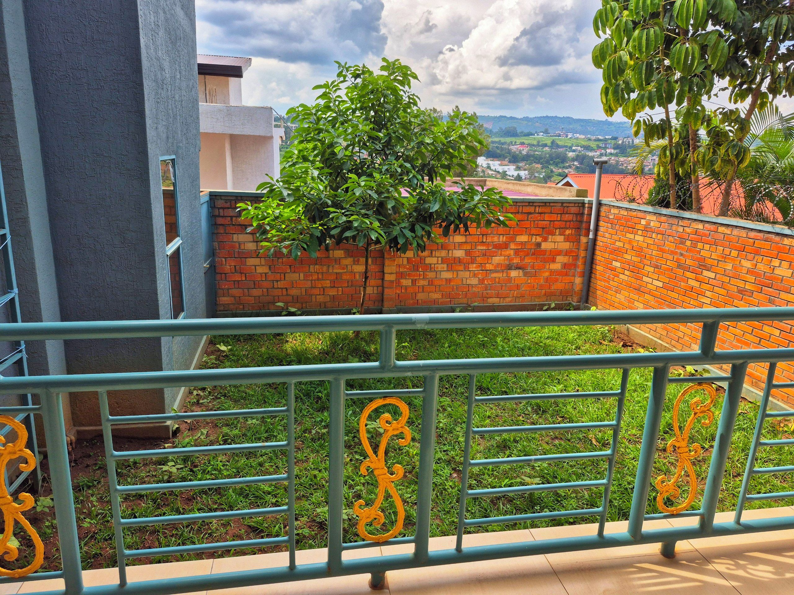 Ein Balkon mit Metallgeländer, einer Ziegelwand und Blick auf eine entfernte Landschaft.