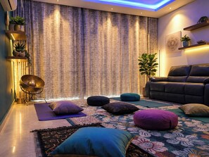A modern living room with a large curtain, a black sofa, and a meditation area with cushions and a mat.