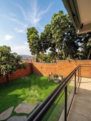 A backyard with a brick wall, a grassy lawn, and potted plants.