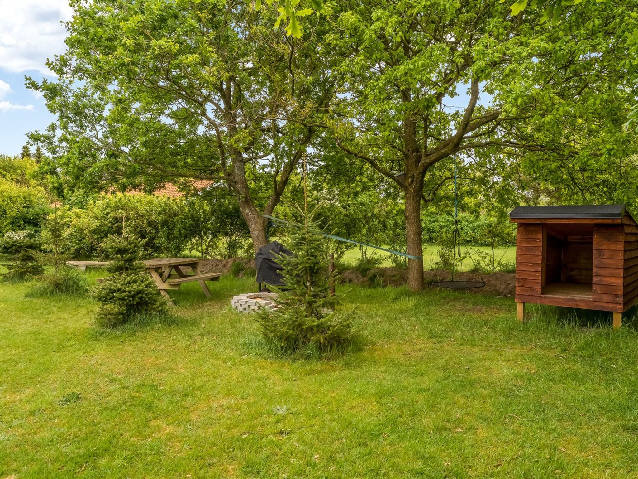 Una estructura de madera con un banco y un pequeño árbol en un área cubierta de césped.