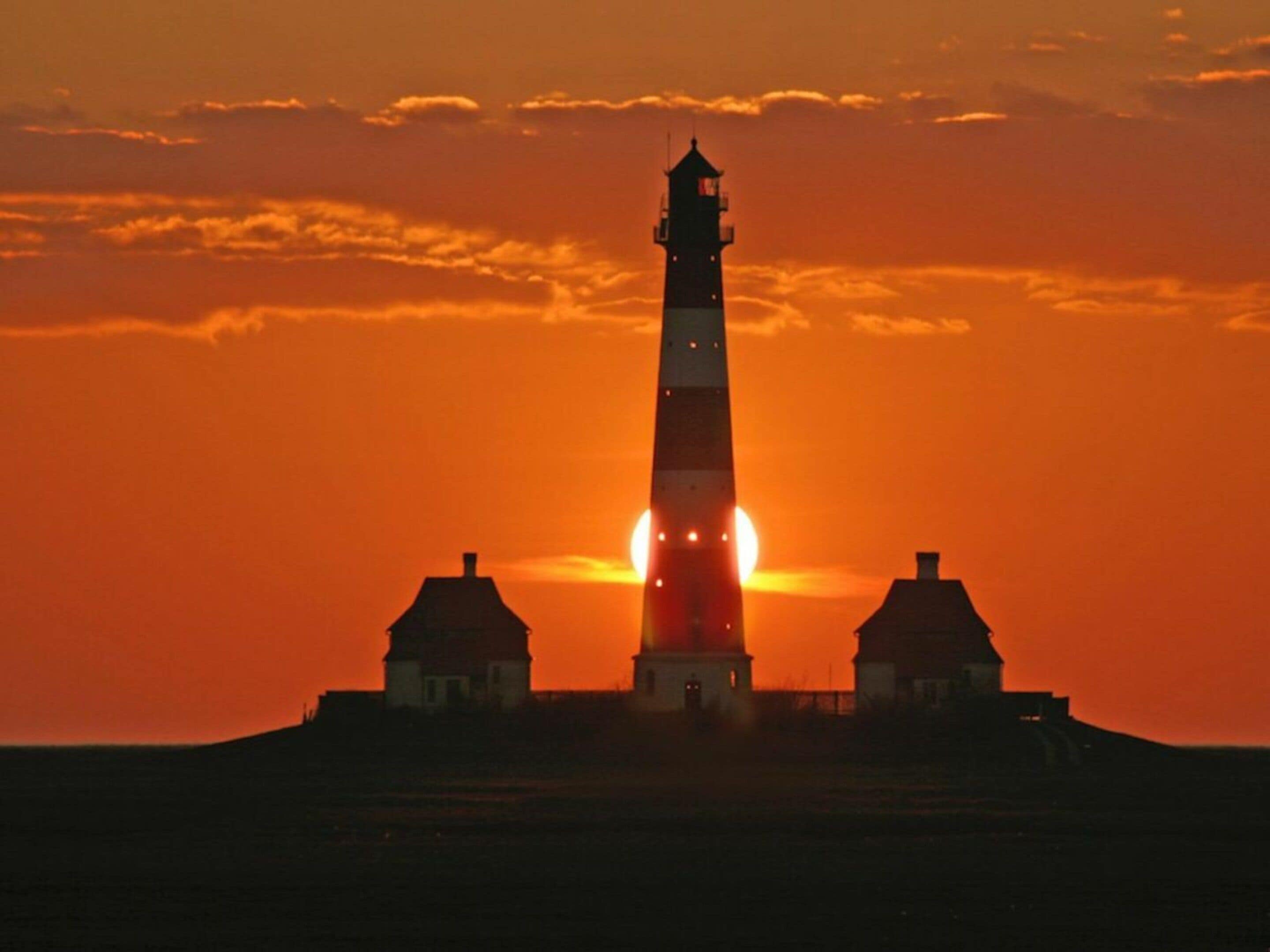 A lighthouse silhouette against a sunset sky.