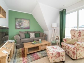 A modern living room with a green accent wall, a sofa set, a coffee table, a floral armchair, and a lamp. - SPO Beach House 3 (St. Peter-Ording)