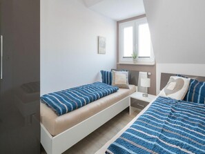Ein Schlafzimmer mit zwei Betten, einem Nachttisch, einer Lampe und einem Fenster mit einer Pflanze.