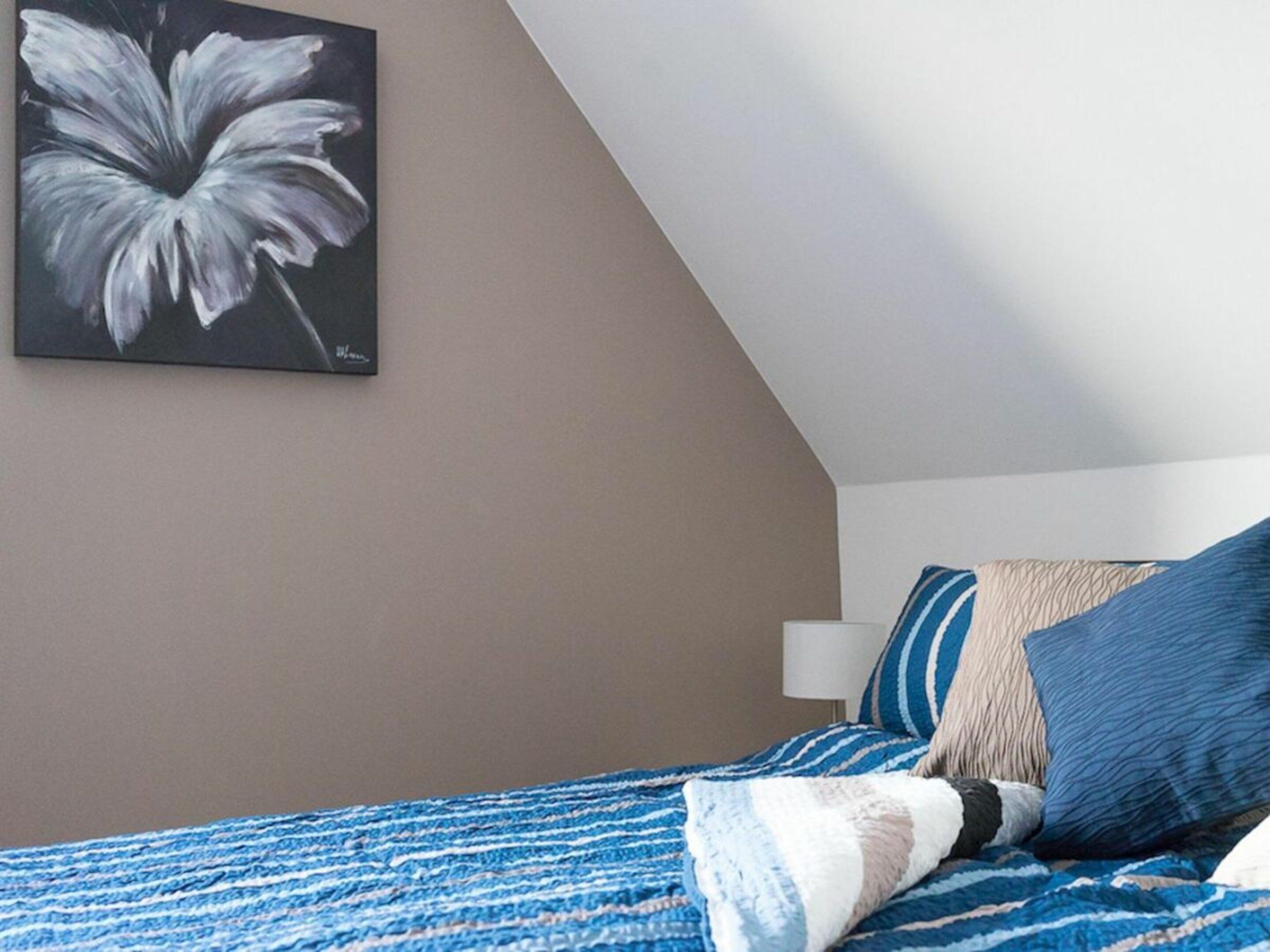 Un dormitorio con cama, almohadas, manta y un cuadro en la pared.