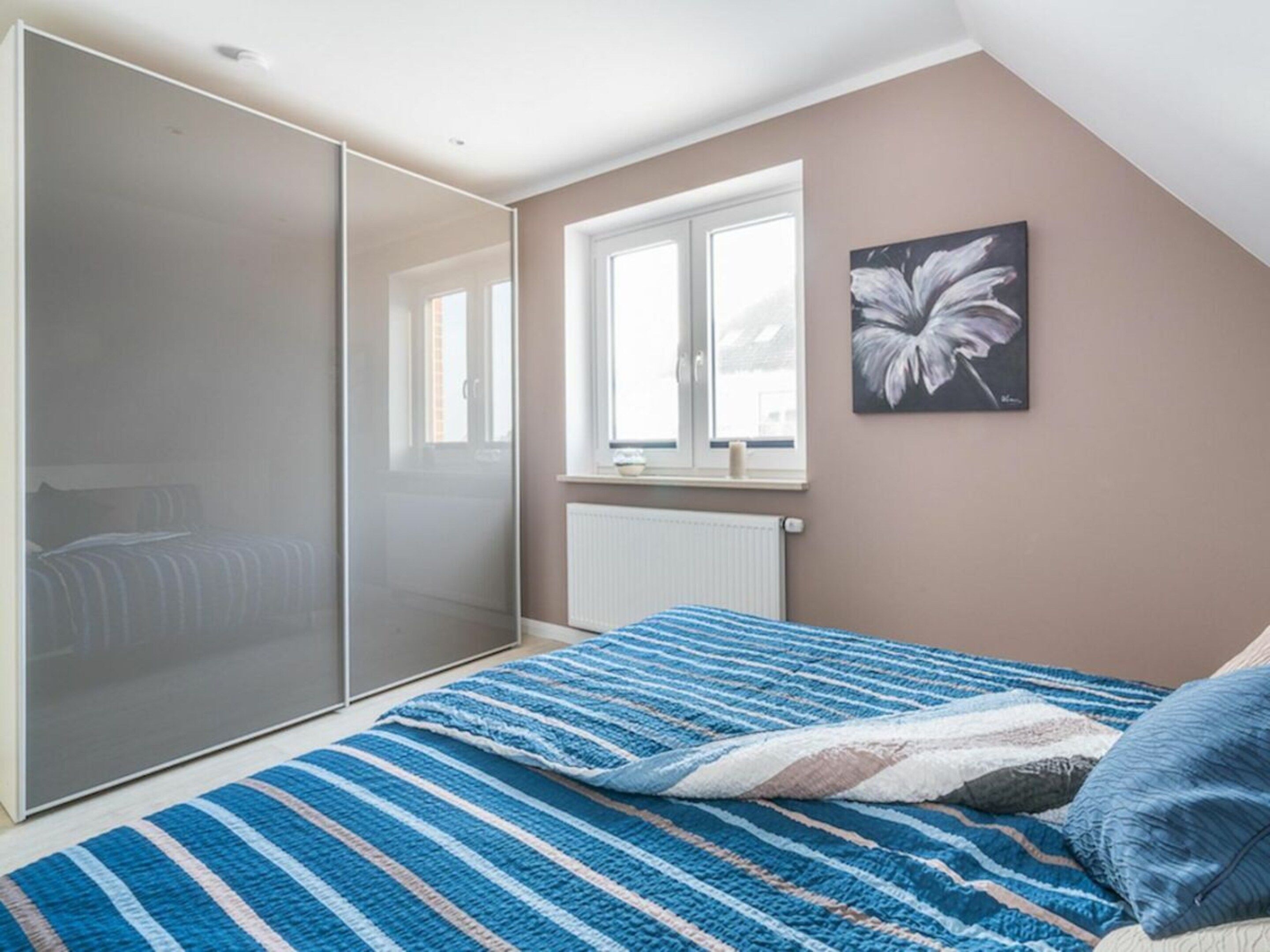 Una camera da letto con un letto, una finestra, un termosifone e un quadro appeso al muro.