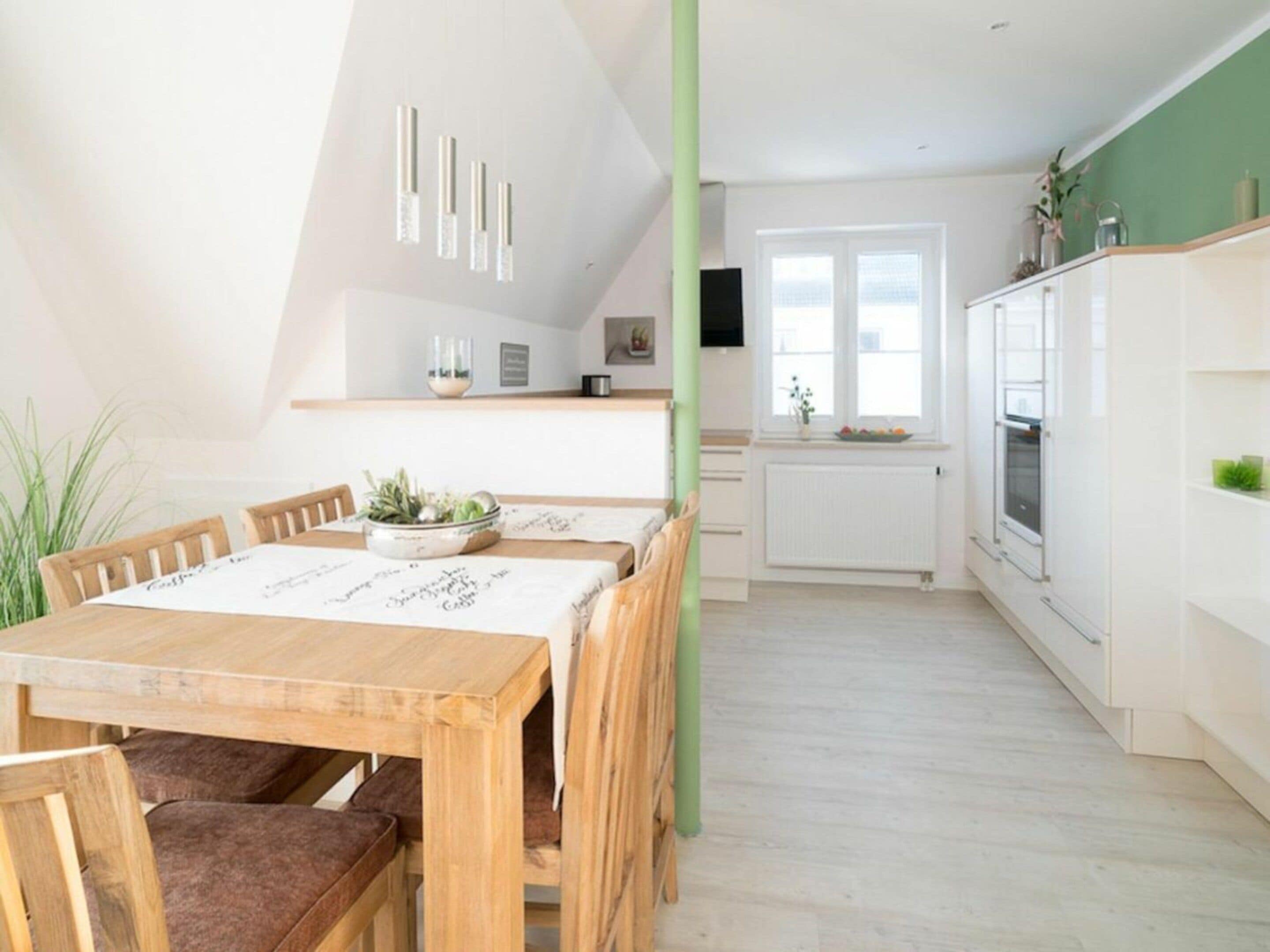 A modern kitchen with white cabinets, a dining table with chairs, and a window with a view.
