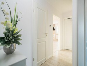 Ein Flur mit einer weißen Tür, einem Blumentopf und Blick in einen Raum mit Küchenzeile.