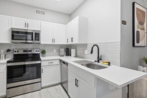 A modern kitchen with white cabinetry, stainless steel appliances, a built-in microwave, and a sink with a black faucet. - Location • Pool • Lux Gym • Free Parking • Cozy Retreat • Fireplace (Phoenix)