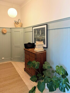 A room with a wooden dresser, a framed picture, a hat on the wall, and a plant.